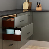 Open kitchen drawer with plates and closed drawers, knife block, and cutting boards on a dark countertop.